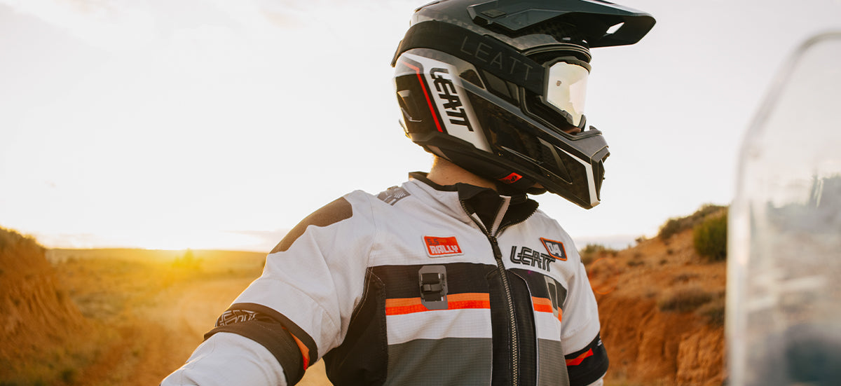 Person wearing a helmet and racing suit in a desert setting with sunset